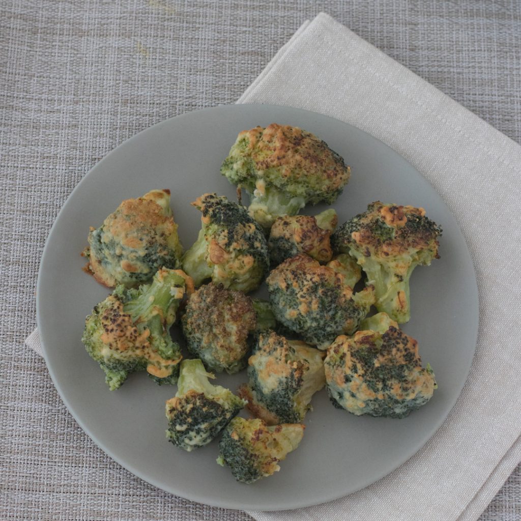 Plato gris con los arboles de brócoli rebozados con un tono tostado. Todo sobre servilleta y mantel gris.
